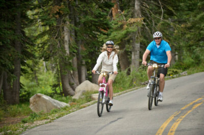 Couple riding Optibikes onroad in a forested area